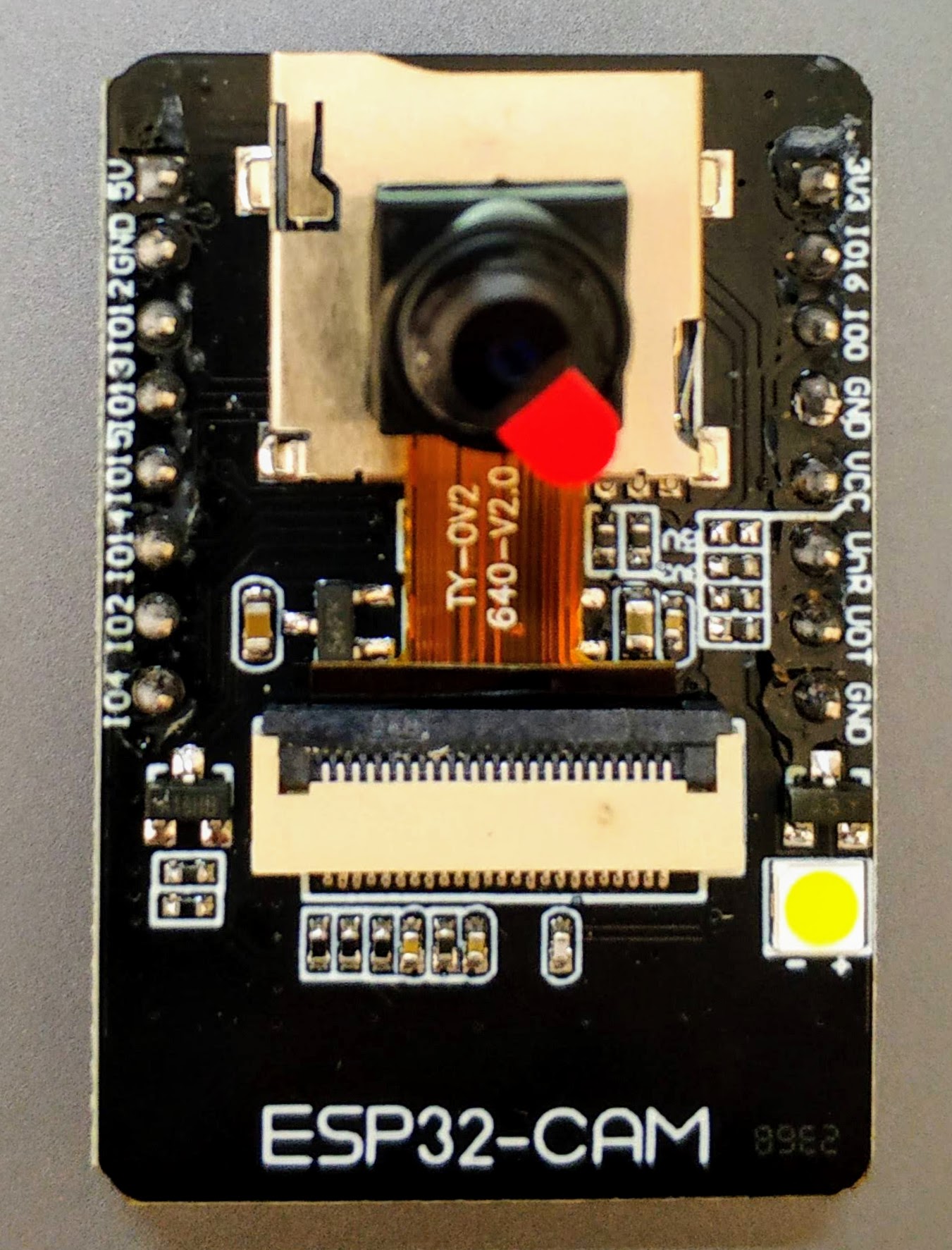 ESP32-CAM board with camera lens, ribbon cable and flash LED
